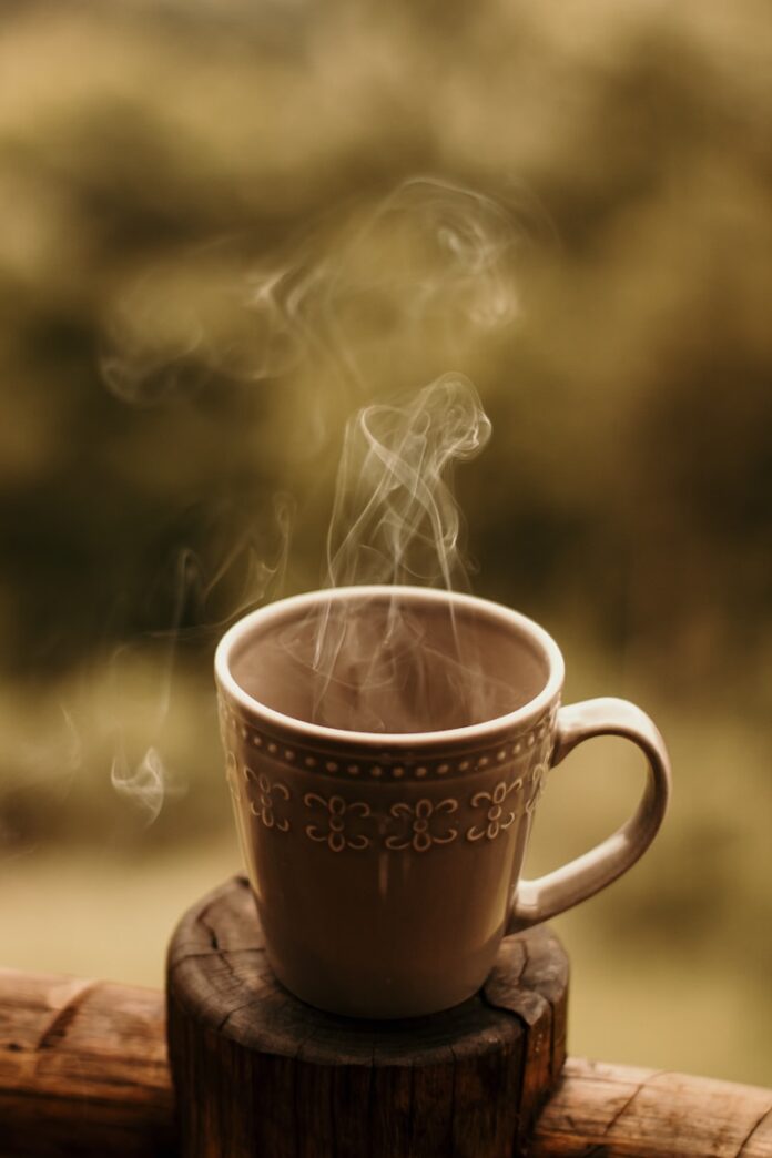 Photo by Nicole Queiroz a steaming cup of coffee sitting on top of a wooden table
