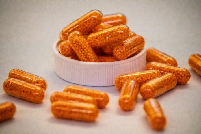 Orange capsules filled with small beads spill from container.